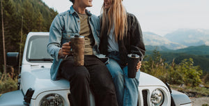 a couple sitting on the hood of a car in the mountains.